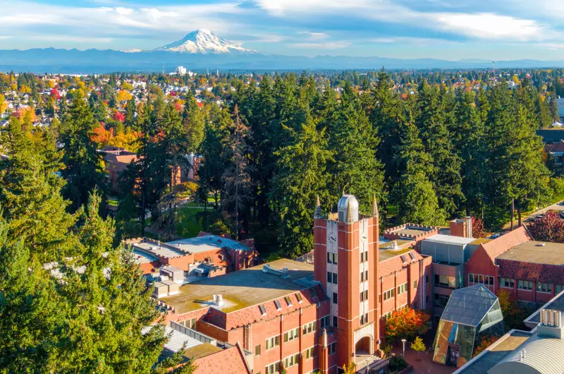Aerial view of a red brick clocktower amongst trees with Mount Rainier in the background.