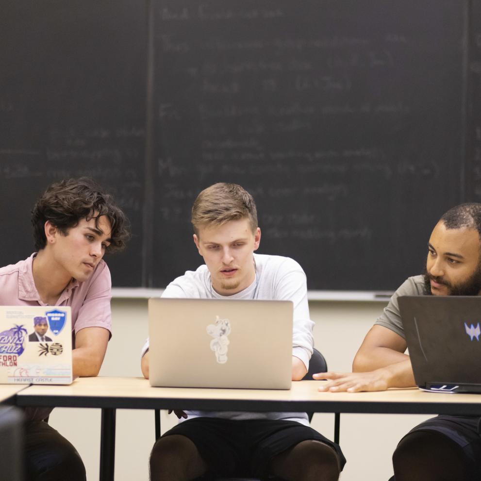 Three students with laptops collaborate on an interdisciplinary summer research project.