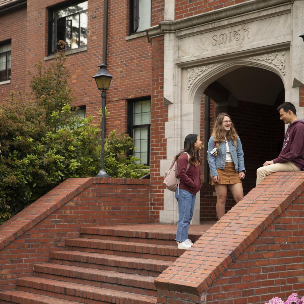 Students stand on the brick steps of a campus building.
