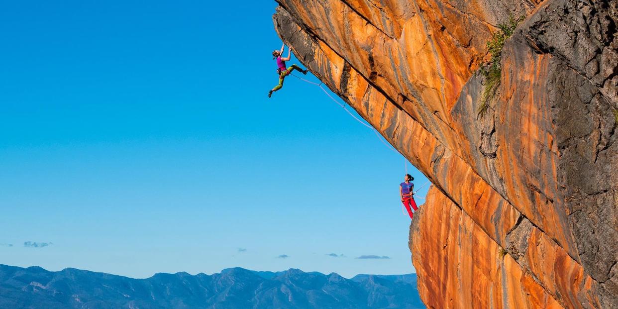 Rock climbers ascend a red rock wall.