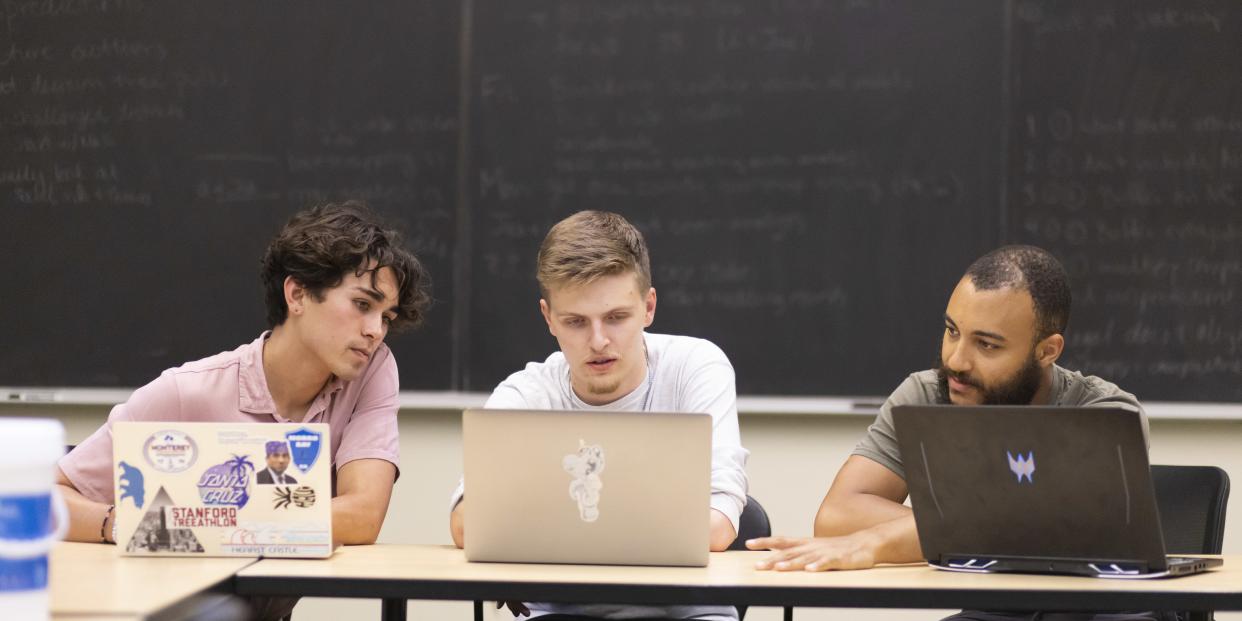 Three students work on laptops during an interdisciplinary summer research project.