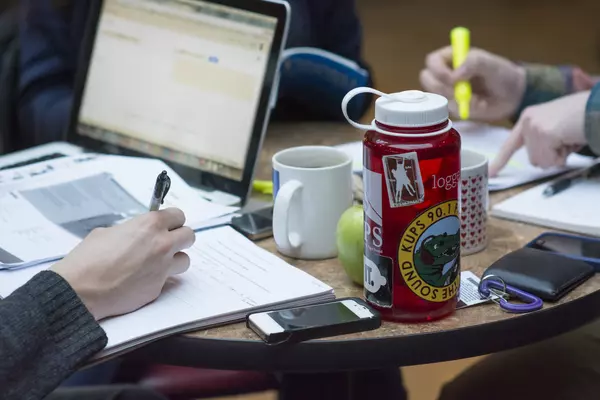 Student taking notes at a table with a laptop and water bottle