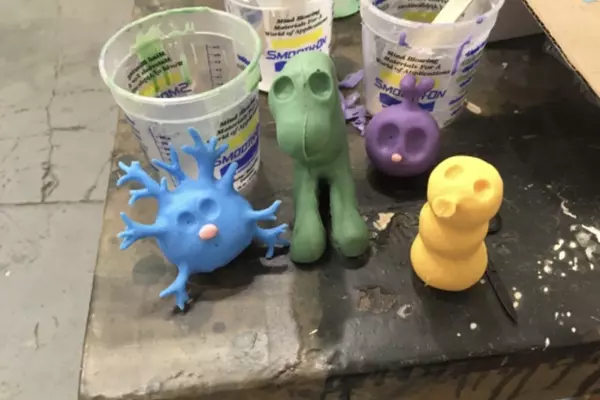 Blue, green, purple, and yellow claymation figures sit on the corner of a work table