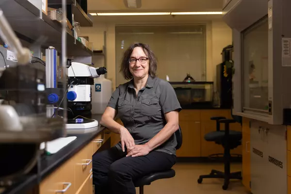 Professor of Biology Leslie Saucedo sits beside a microscope in her lab.