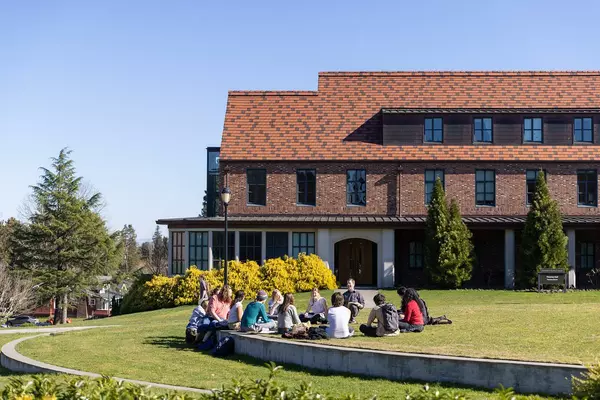A group of student sit in the grass around an instructor. 