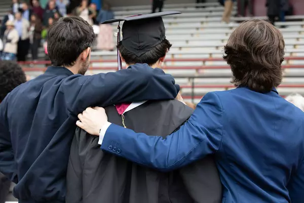 Two men on either side of a graduate put their arms on his shoulders 