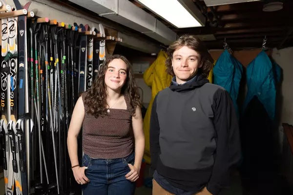 Claire Bargman ’26 and Reggie Westgate ’27 in front of a row of skis at the Expeditionary.