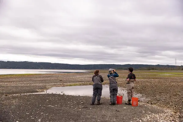 Three people stand at low tide looking toward the Puget Sound