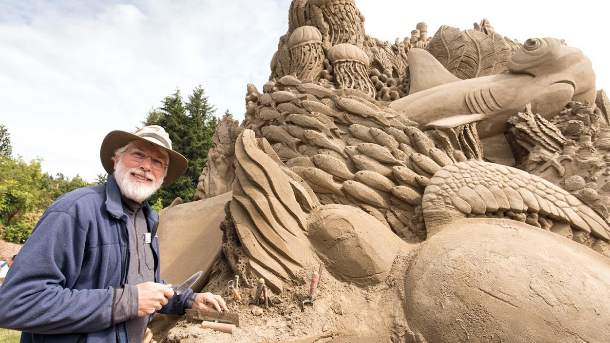 Jeff Strong smiling in front of his sand sculpture