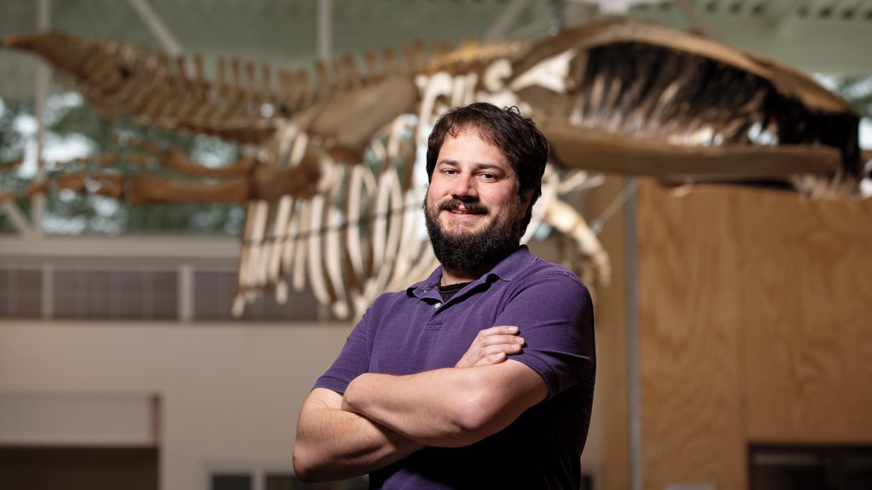 Matt Lonsdale ’08, M.A.T.’09, standing in front of a whale skeleton displayed in the science center