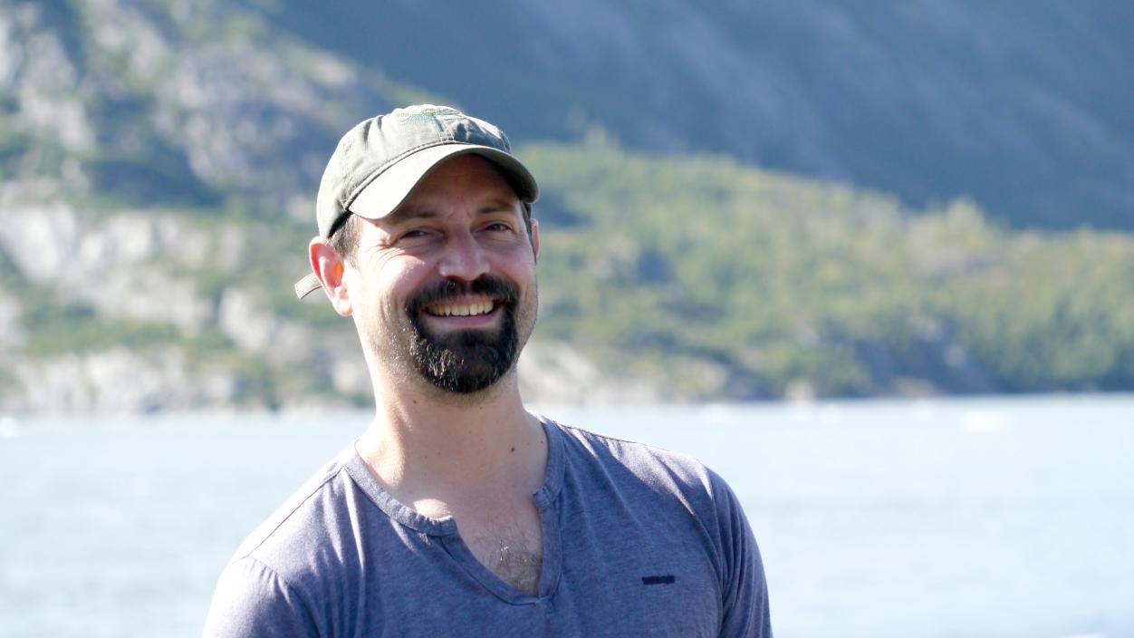 Man in a blue shirt smiling with a lake in the background