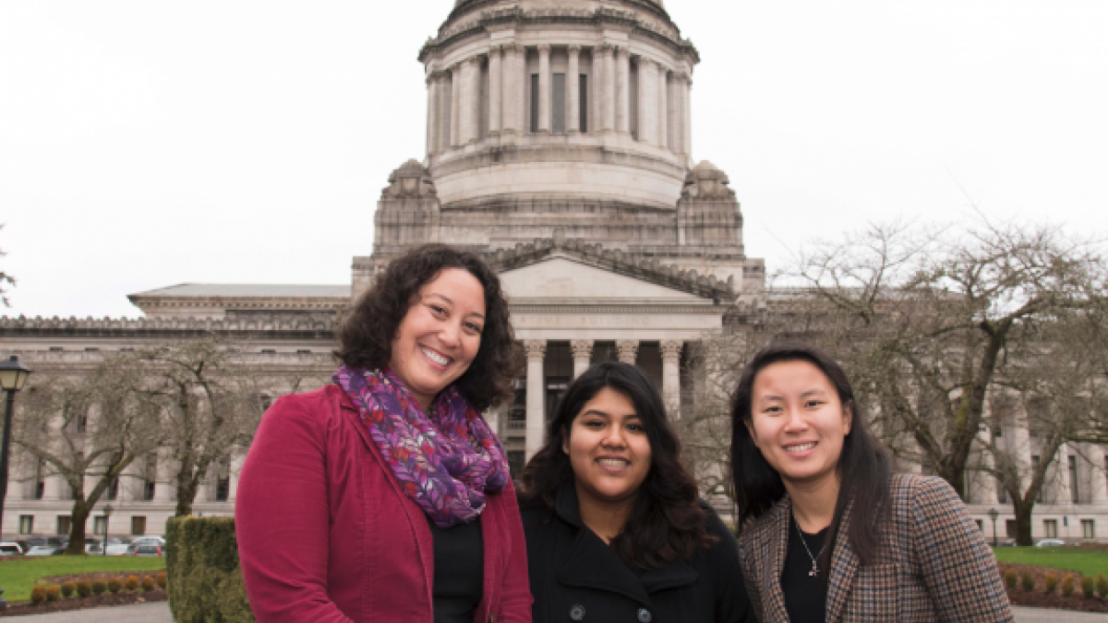 Three people smiling in front of the state capitol building