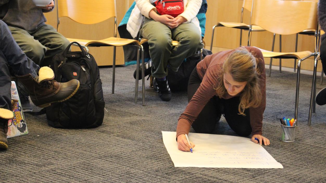 A person sitting on the floor writing on a poster board