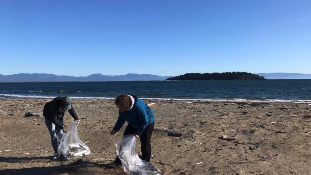 Two people cleaning up trash on a beach