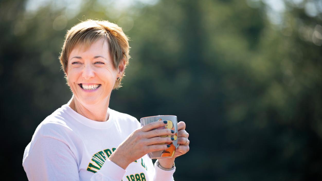 A person outdoors smiling and holding a mug