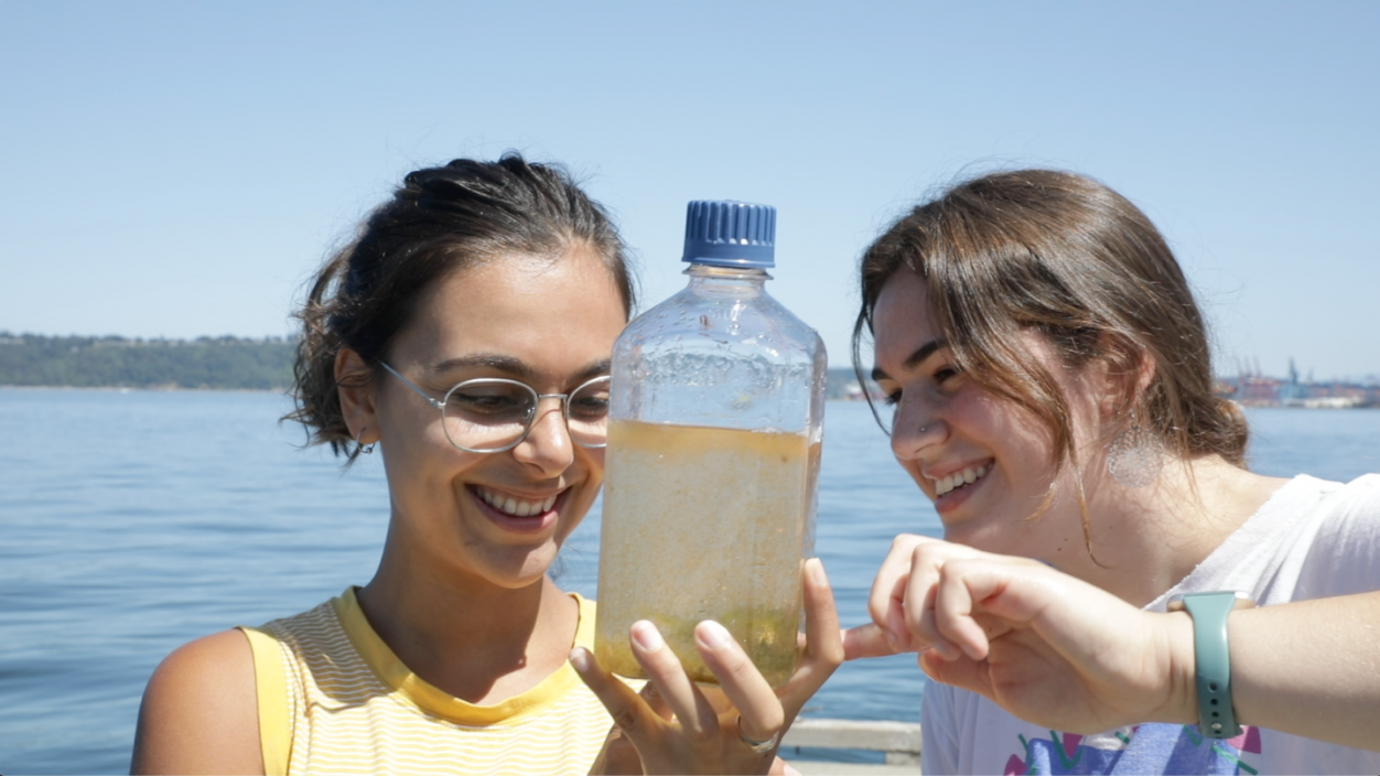 Two female students examine a bottle filled with water from the Puget Sound
