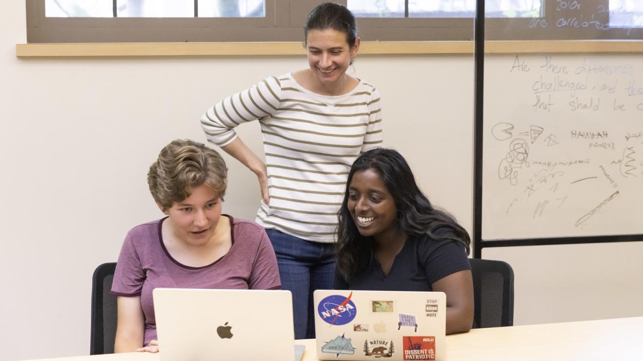 Prof. Courtney Thatcher stands behind students working on their laptops during class