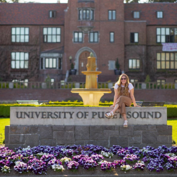 Student sitting on University of Puget Sound sign