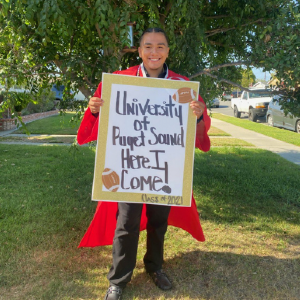 Student wearing red graduation gown holding sign that says "University of Puget Sound here I come" 