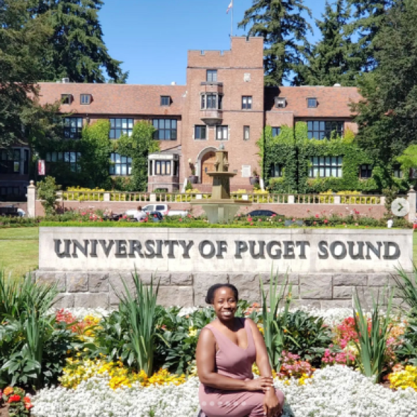 Alumni sits in front of Puget Sound sign