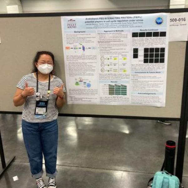 Student gives thumbs up in front of research poster