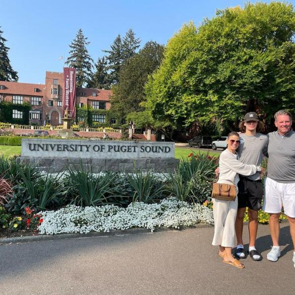 Parents flank a Puget Sound student in front of the university sign on Jones Circle