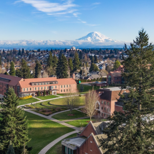 An aerial view of the Puget Sound campus featuring the Warner Hall, the Event Lawn, Thomas Hall, and Mount Rainer in the background.