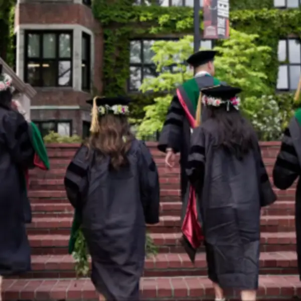 Four graduates walking up the steps in front of Jones Hall on graduation day.