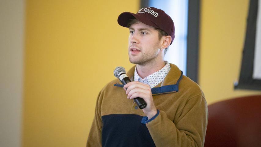 Man speaking into a microphone and wearing a Puget Sound hat