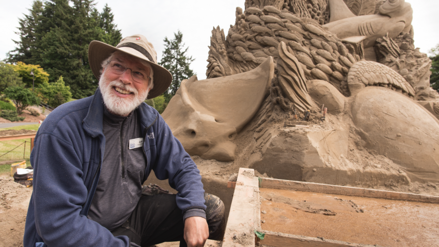 Jeff Strong smiling next to his sand sculpture and tools