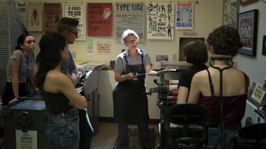 A person instructing a small group on how to use a letterpress printer