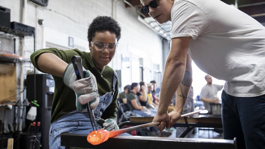 Two people using glass blowing equipment