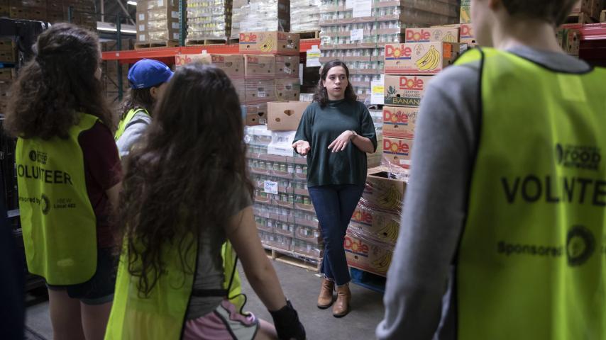 A person in front of food crates talking to a small group of people