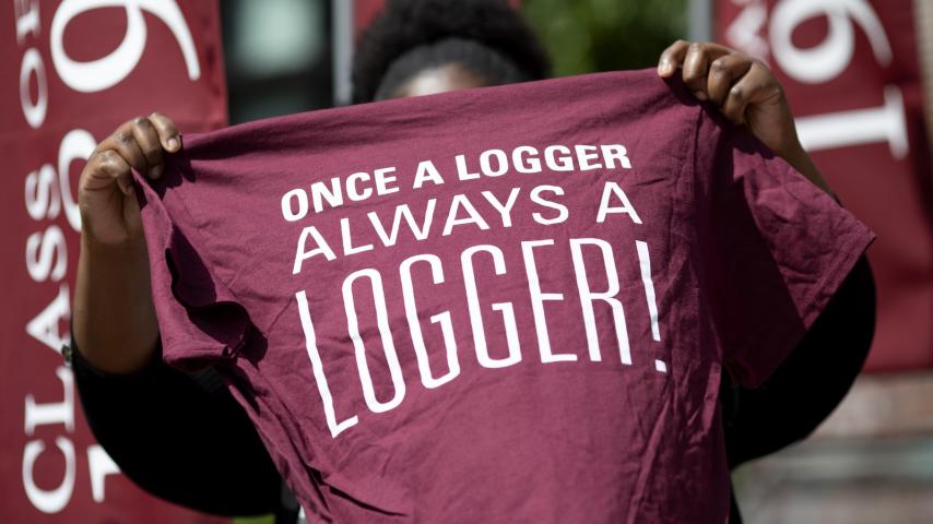 Student holding up a maroon t-shirt that says Once a Logger, Always a Logger!