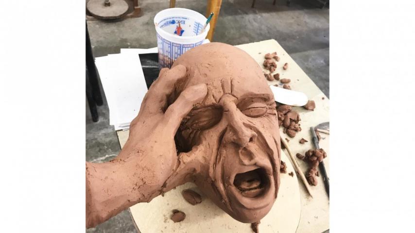 Clay sculpture of face with a hand on its right side