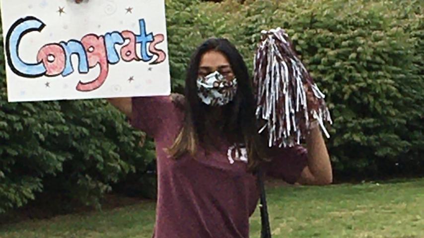 A student holds up a sign reading "Congrats!" and a maroon and white pompom