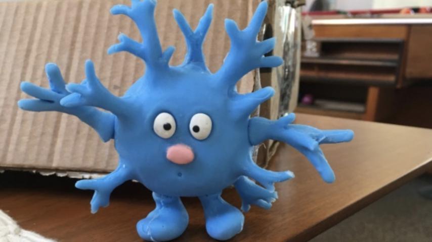 A blue clay figure, one of the characters from "The Cortex Crew" stands on the edge of a table