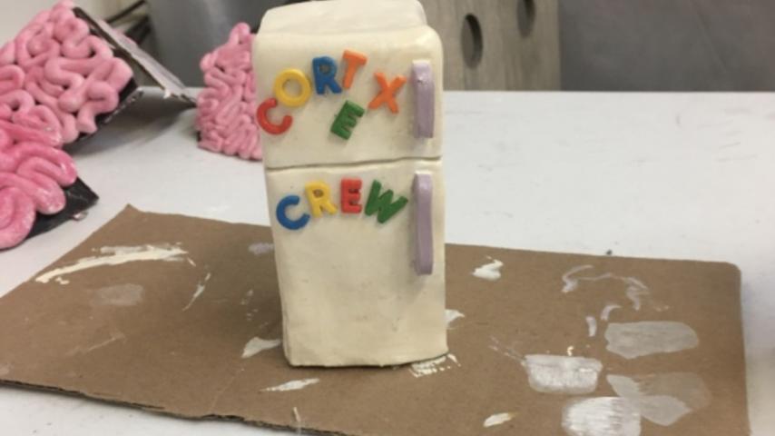 Clay figure of a white refrigerator with "Cortex Crew" in colorful letters on the front