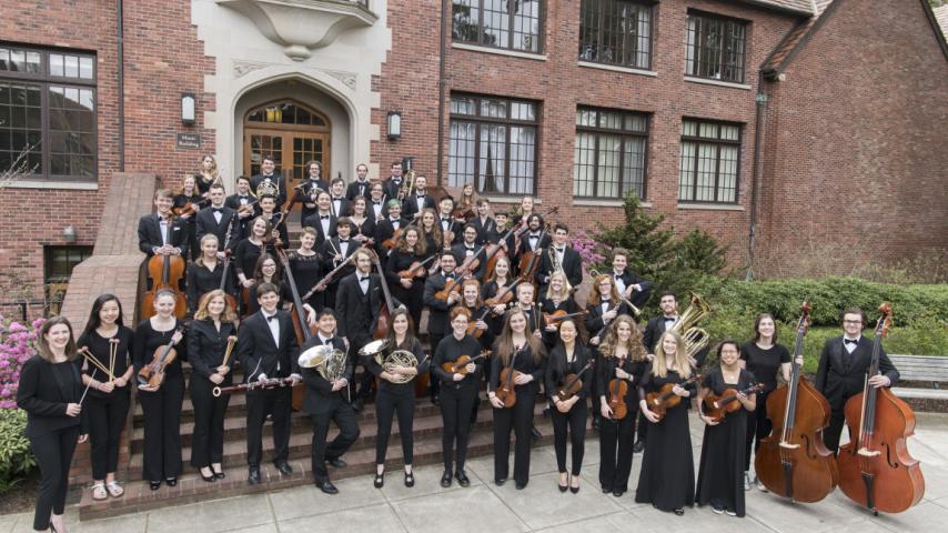 Symphony Orchestra members with instruments outside a university building