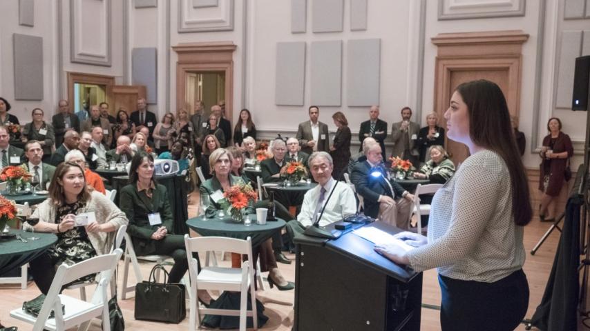 A person addressing a room of people seated at tables