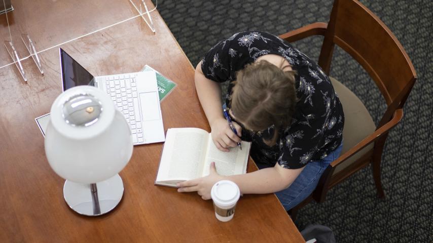 Chloe Shankland sits at a table in Collins Memorial Library, making notes in a book of poetry