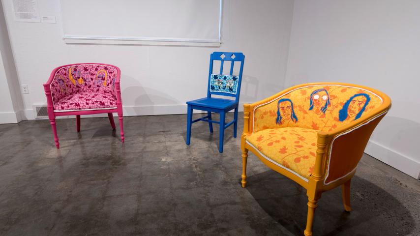 A display of three colorful chairs with artworks painted on them