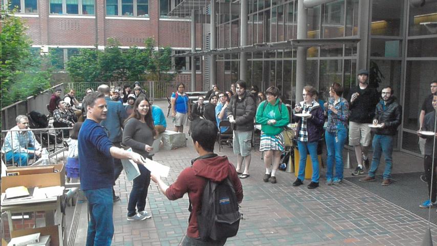 Professor handing paper to student amidst crowd in Thompson courtyard.