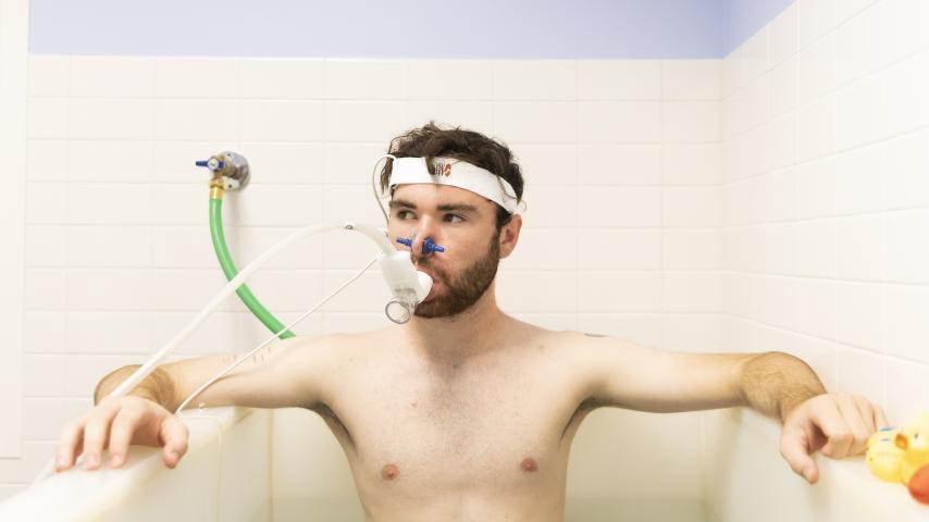 Graham Hall ’24 sits immersed up to his chest in a tub of water while wearing a headband which monitors his vitals and a breathing apparatus.