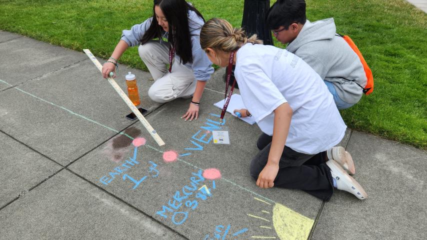 Students kneeling on sidewalk with a scientific chalk drawing