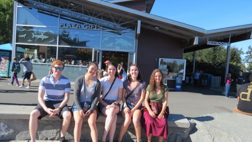 Five people sitting on a bench in front of a gift shop.