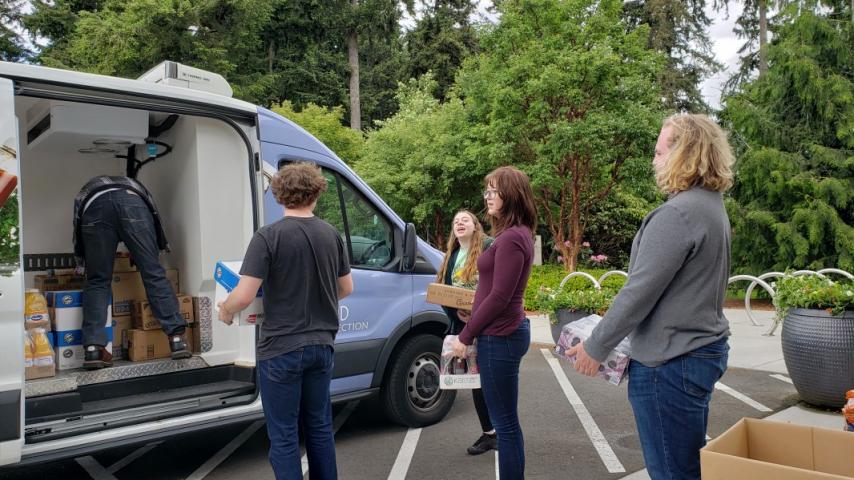 Five people carrying boxes into a van.