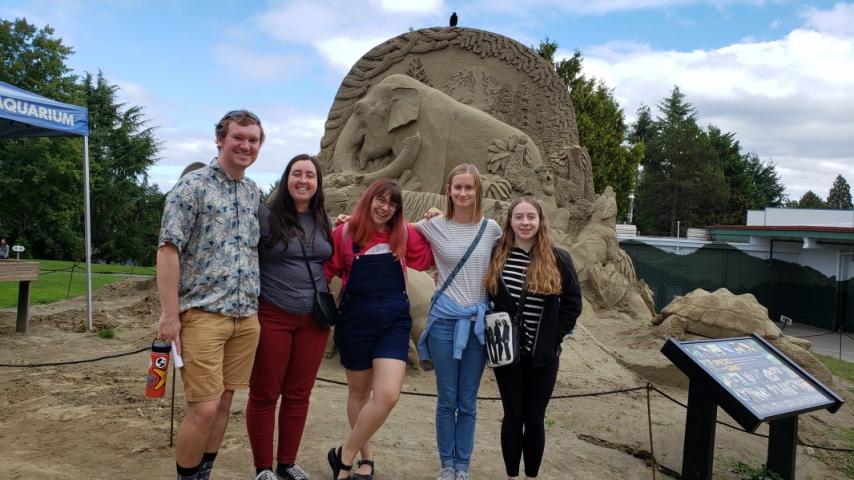 Five people standing in front of a sand scuplture.
