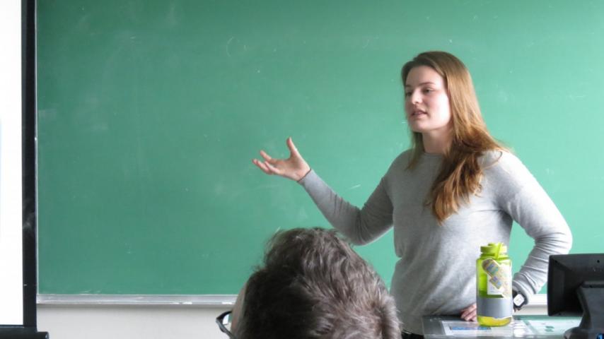 A person speaking in front of a chalkboard.