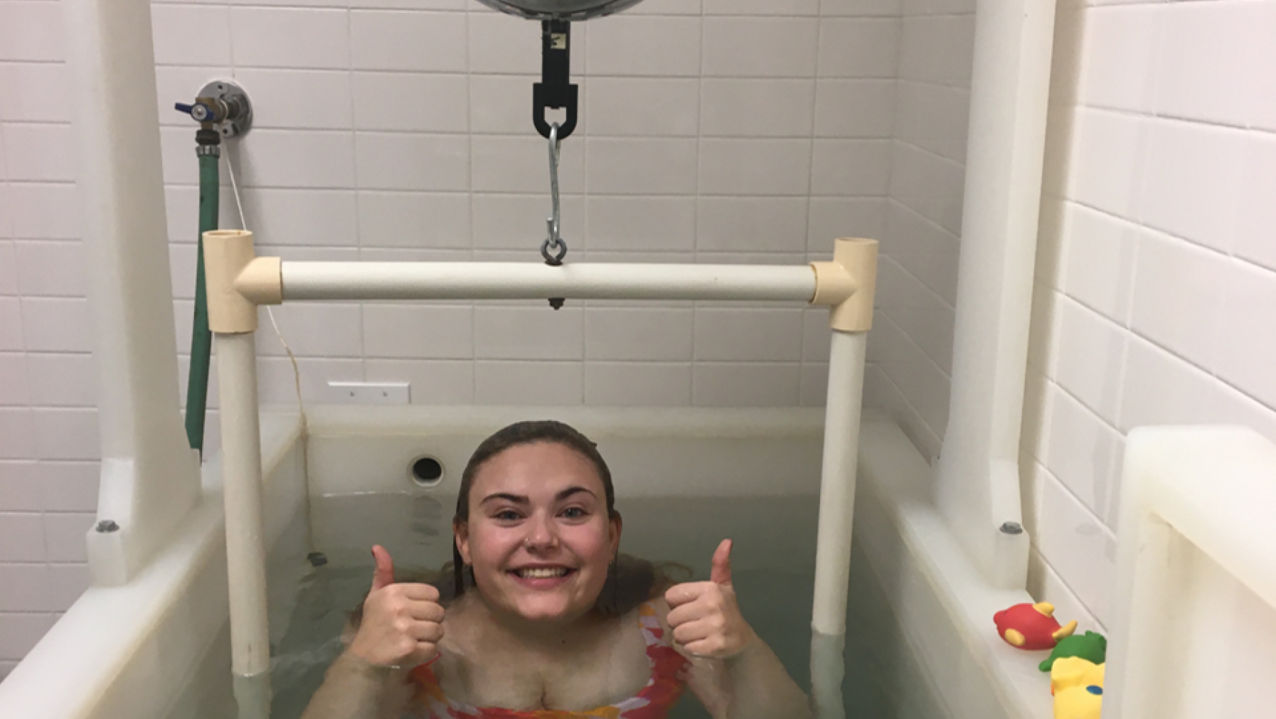 A person smiling and holding their thumbs up in water.